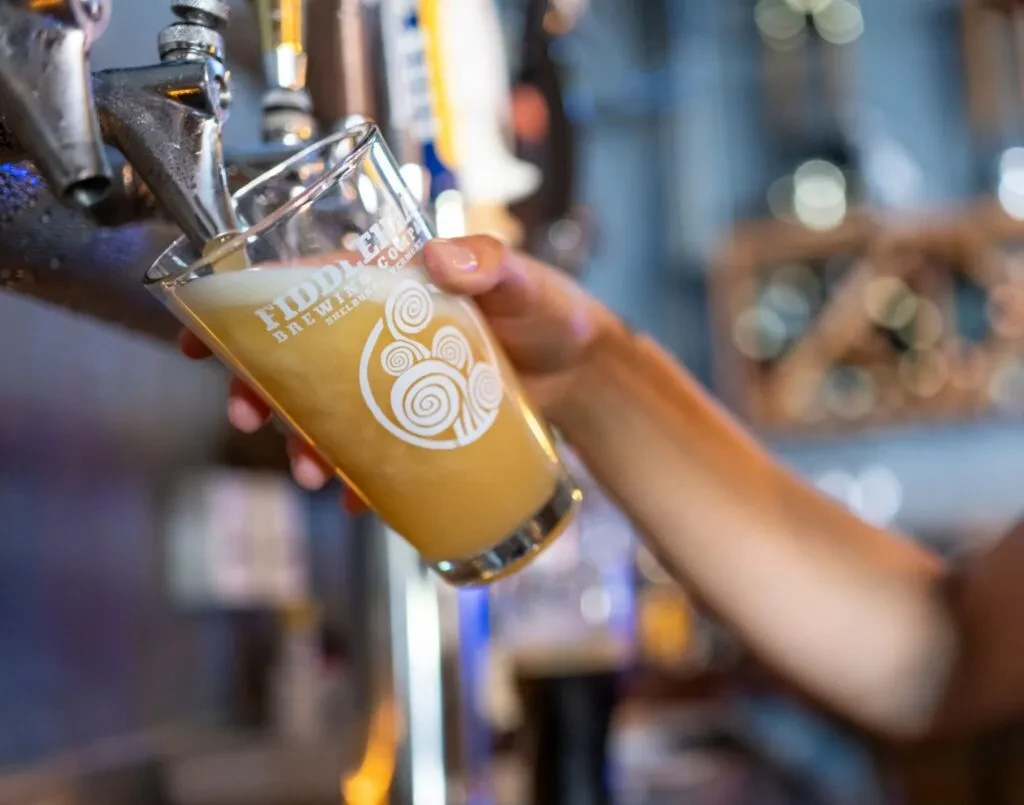 Hand pouring Fiddler Brewing Co. amber beer from a chrome tap.