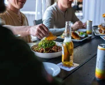 Hand dips tortilla chip into meat and guacamole with drinks.