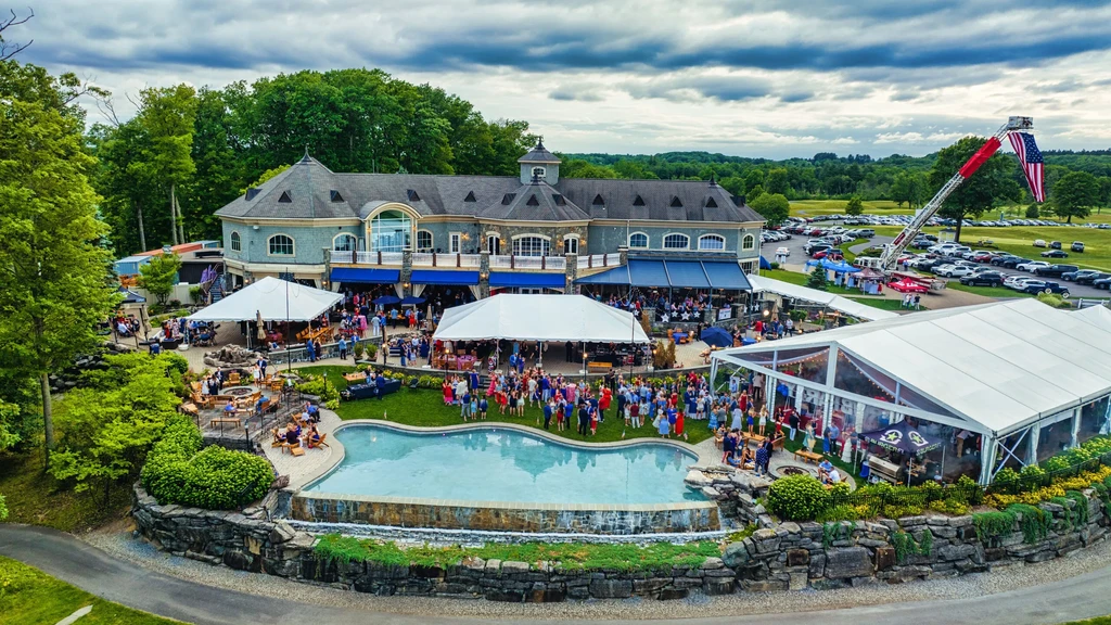 Aerial view of elegant building, outdoor event with tents, pool, American flag.
