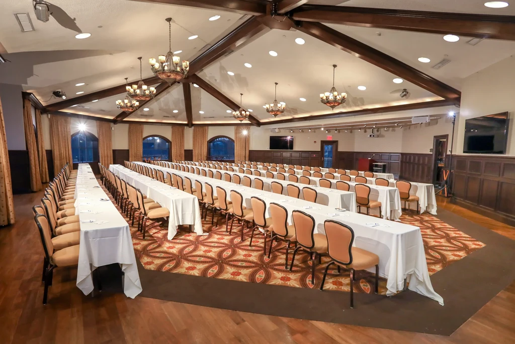 Empty, elegant banquet hall with vaulted ceiling, set tables, and presentation area.
