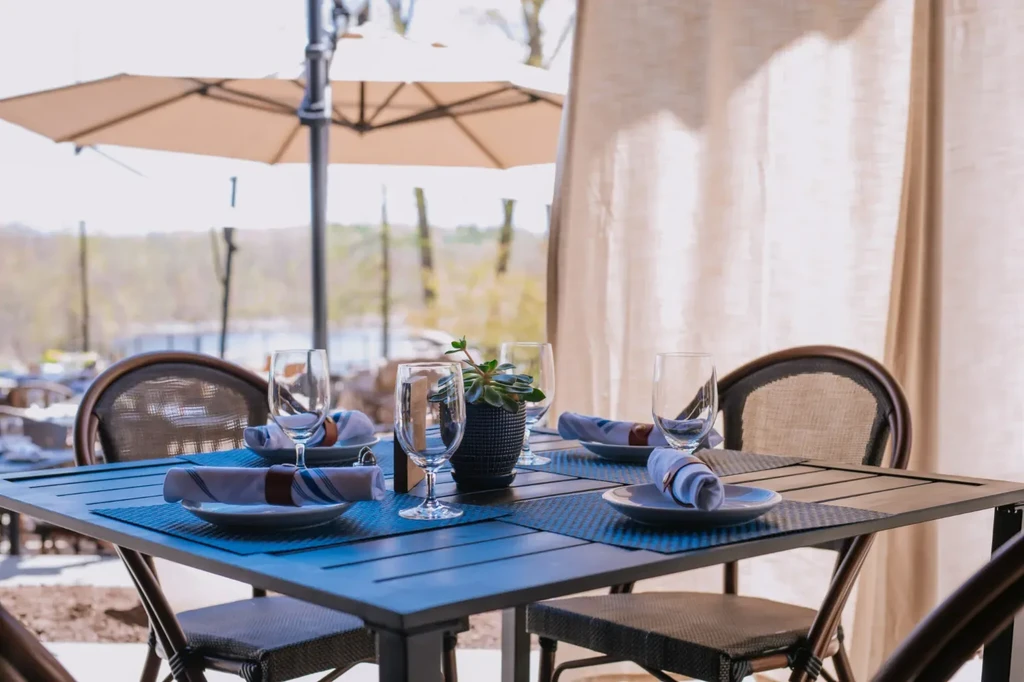 Outdoor dining table for four with succulent, overlooking water and trees.