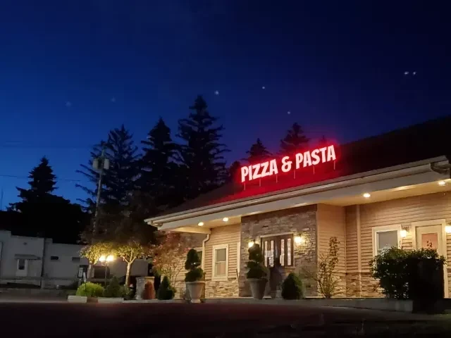 Well-lit 'PIZZA & PASTA' restaurant exterior, stone facade, red neon sign.
