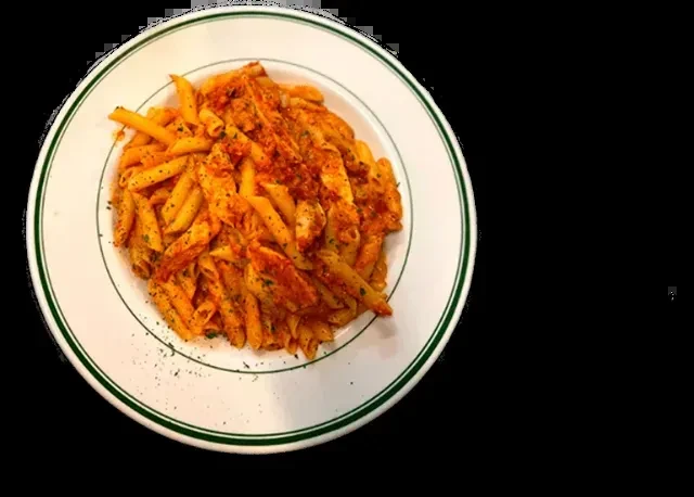 Penne pasta with reddish sauce, chicken, and herbs on a white plate.