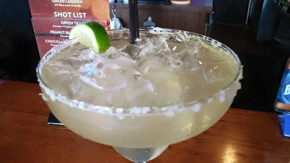 Salt-rimmed margarita with lime wedge and straw on wooden bar.