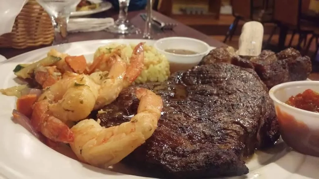 Steak, shrimp, rice, vegetables, and sauces on a plate in a restaurant.