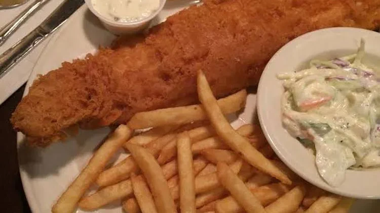 Overhead view of crispy fish, golden fries, coleslaw, and white sauce.