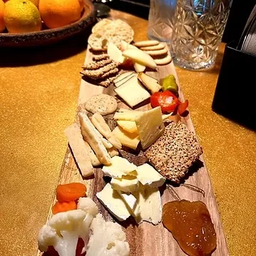 Overhead charcuterie board with cheeses, crackers, dried fruit, pickled vegetables.