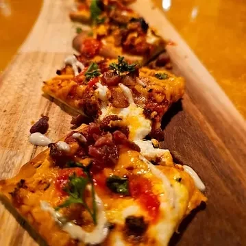 Flatbread slices with cheese, bacon, and herbs on a wooden board.