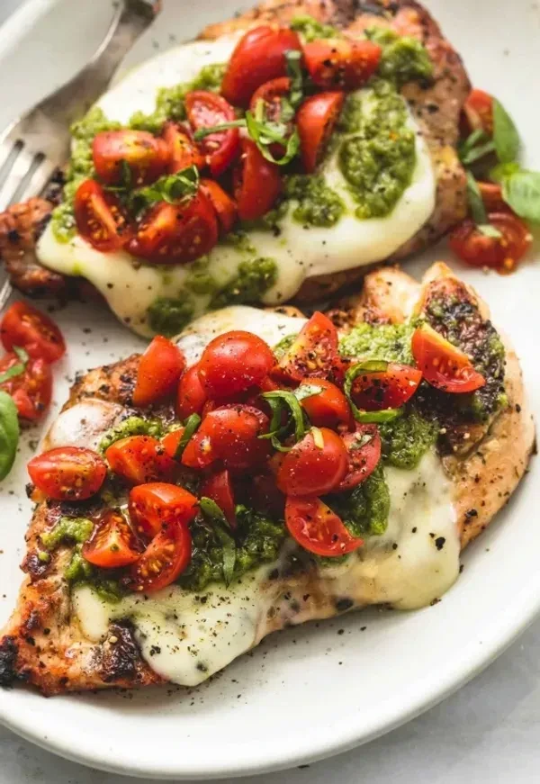 Chicken breasts with melted cheese, pesto, tomatoes, and basil.