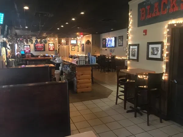 Dimly lit sports bar interior with booths, bar, sports jerseys, and TVs.