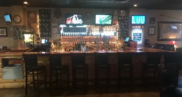 An empty, rustic bar in "The Tavern" with bottles and TVs.