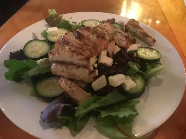 Close-up of grilled chicken salad with mixed greens, cucumber, and feta.