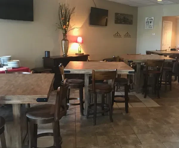Dimly lit casual restaurant with wooden high-top tables and checkered floor.
