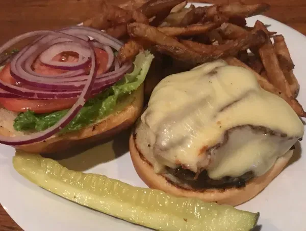 Deconstructed burger with cheese, lettuce, tomato, onions, fries, pickle.