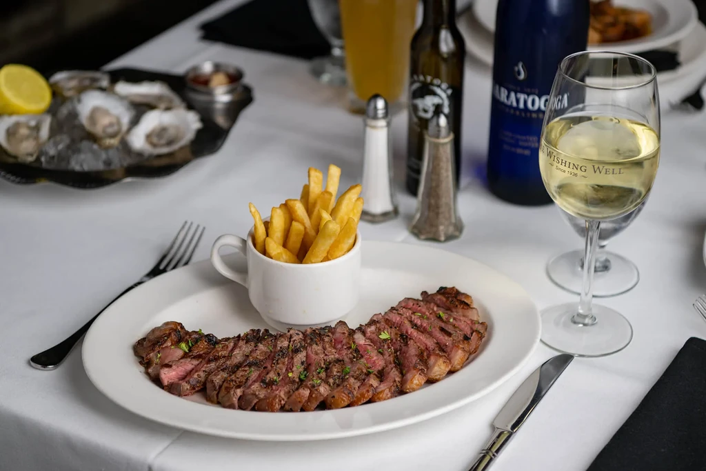Grilled steak, fries, oysters, and wine on a luxurious table.