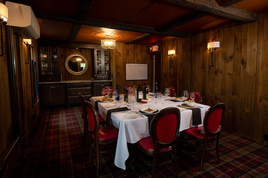Warmly lit private dining room with dark wood, red chairs, set table.