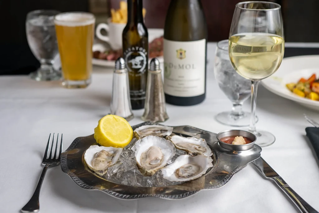 Six fresh oysters on ice, lemon, and sauce on a dining table.