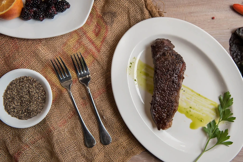 Top-down grilled steak dinner, garnished, on white plate in rustic setting.