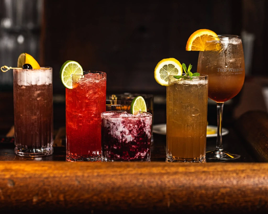 A row of five distinct cocktails on a polished wooden bar.