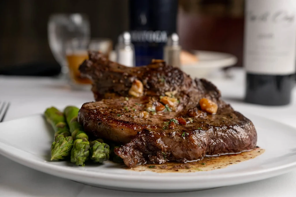 Seared medium-rare steak, asparagus, and herbs on a white plate.