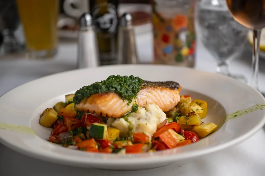 Plated pan-seared salmon with pesto, mashed potatoes, and colorful vegetables.