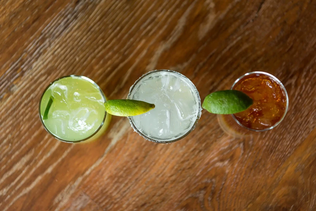 Overhead shot of three cocktails: green, clear, and amber, on wood.