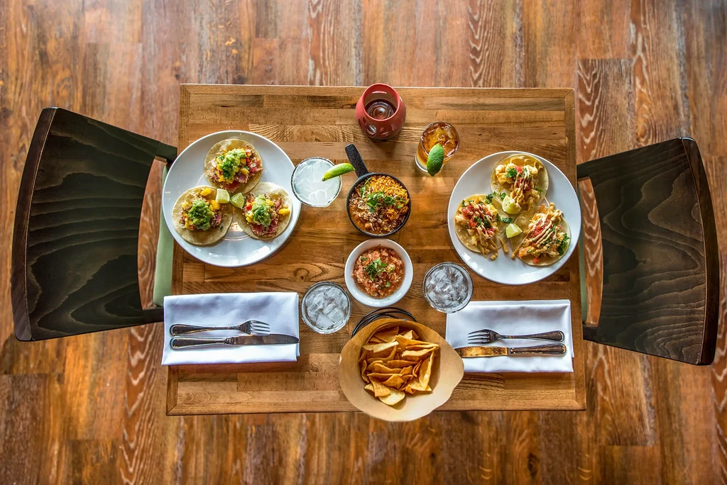 Overhead: Vibrant tacos, rice, chips, and drinks on a wooden table.
