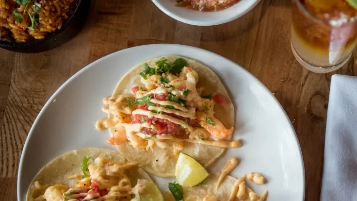 Close-up of shrimp tacos, lime, rice, and drink on wooden table.