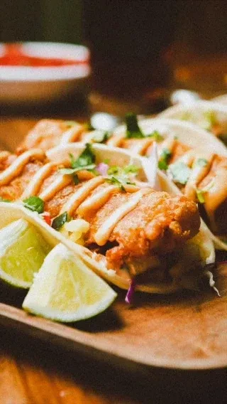 Multiple fish tacos topped with creamy sauce, cilantro, and lime.