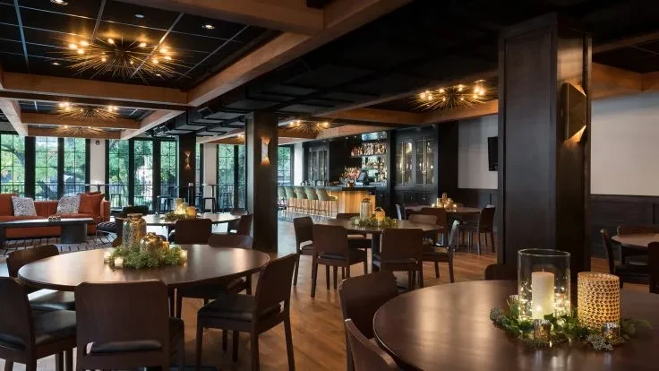 Upscale restaurant interior with dark wood, warm lighting, lounge, and bar.