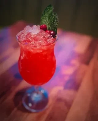 Red cocktail in hurricane glass with crushed ice, cranberries, mint.
