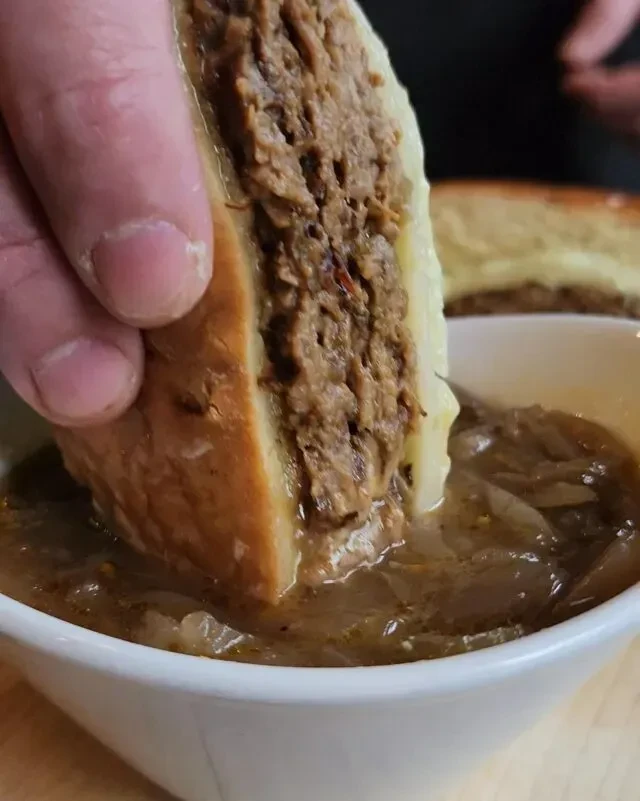 Hand dipping a crusty French dip sandwich into savory onion broth.