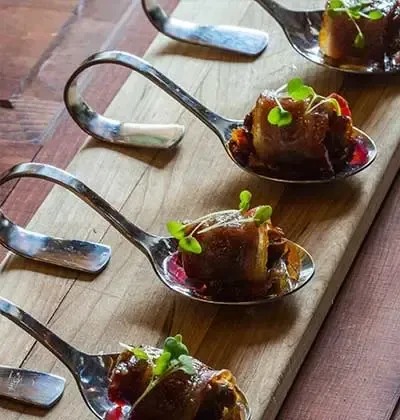 Bite-sized appetizers in silver spoons with microgreens on wood.