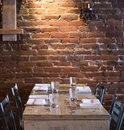 Rustic wooden table set with napkins and glasses against a brick wall.