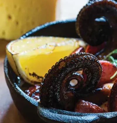 Cooked octopus tentacles and lemon in a cast iron skillet.