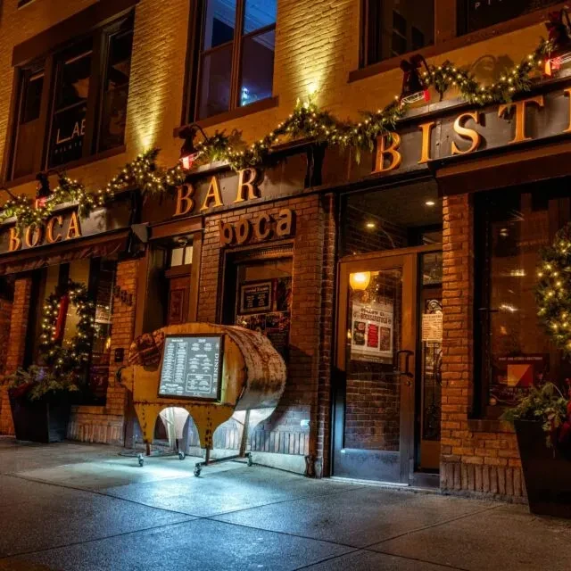 Nighttime illuminated Boca Bar Bistro with festive lights and glowing menu.