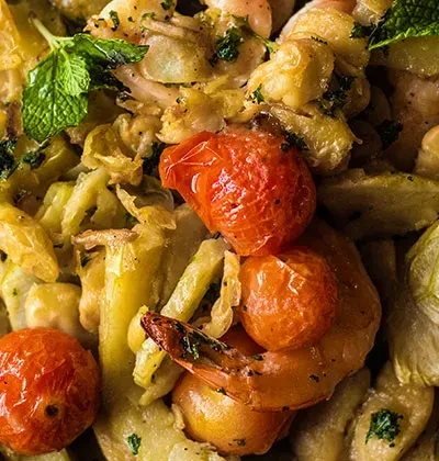 Dish with roasted cherry tomatoes, vegetables, fresh herbs, and charred shrimp.