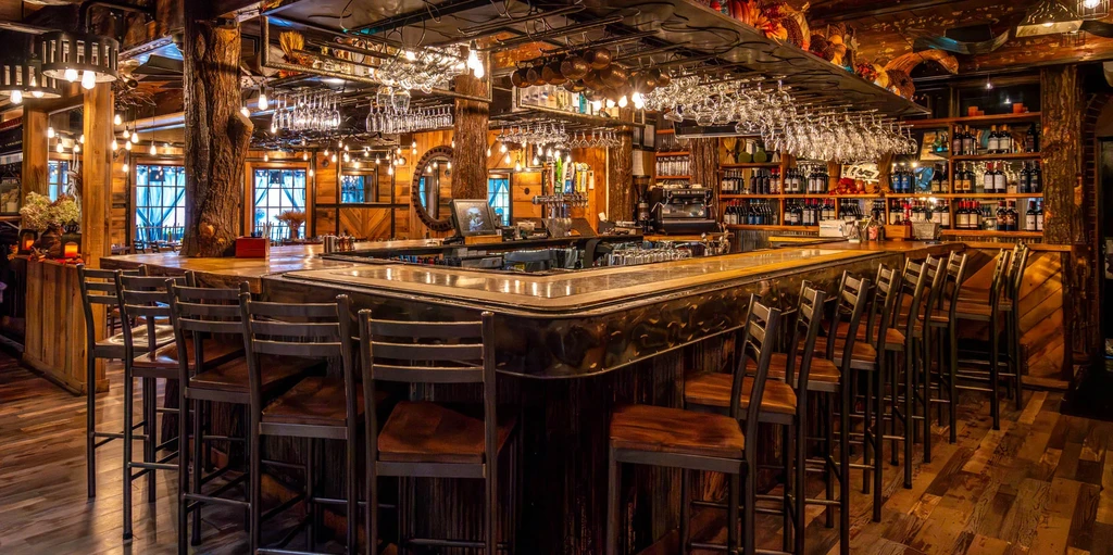 Rustic, warmly lit U-shaped bar with liquor display and wooden pillars.