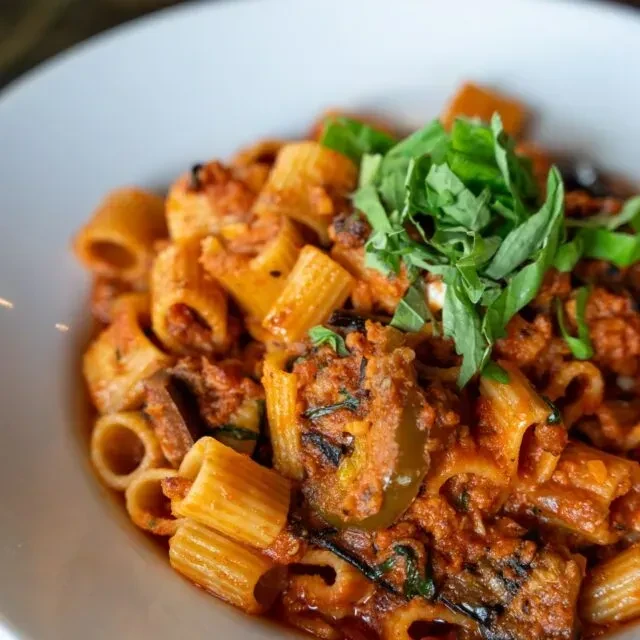Rigatoni pasta with hearty reddish-brown sauce and fresh basil.