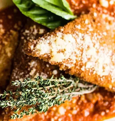 Fried breaded pasta with grated cheese, tomato sauce, and thyme sprig.
