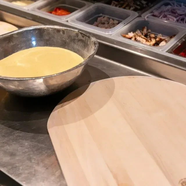 Food prep area with flour bowl, pizza peel, and ingredient containers.