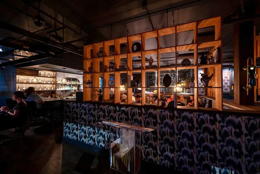 Modern, dimly lit restaurant interior with cubby shelves, bar, and patrons.