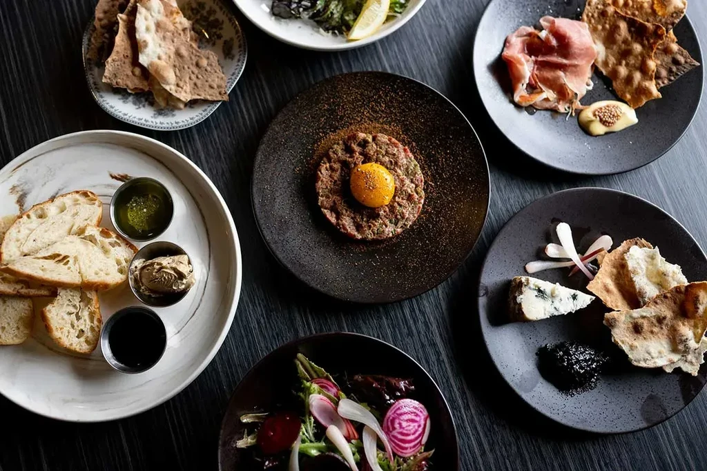 Diverse appetizers on small plates arranged on a dark wooden table.