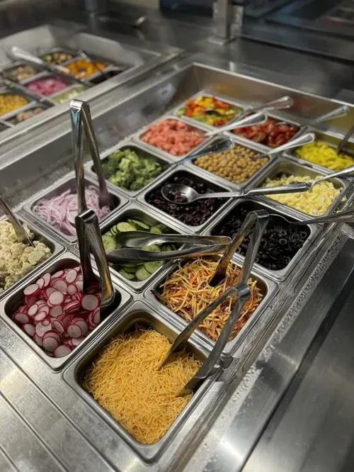 Overhead view of a self-serve salad bar with diverse fresh toppings.