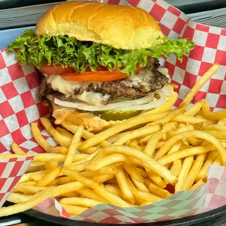 Close-up of a double cheeseburger and fries in a checkered basket.