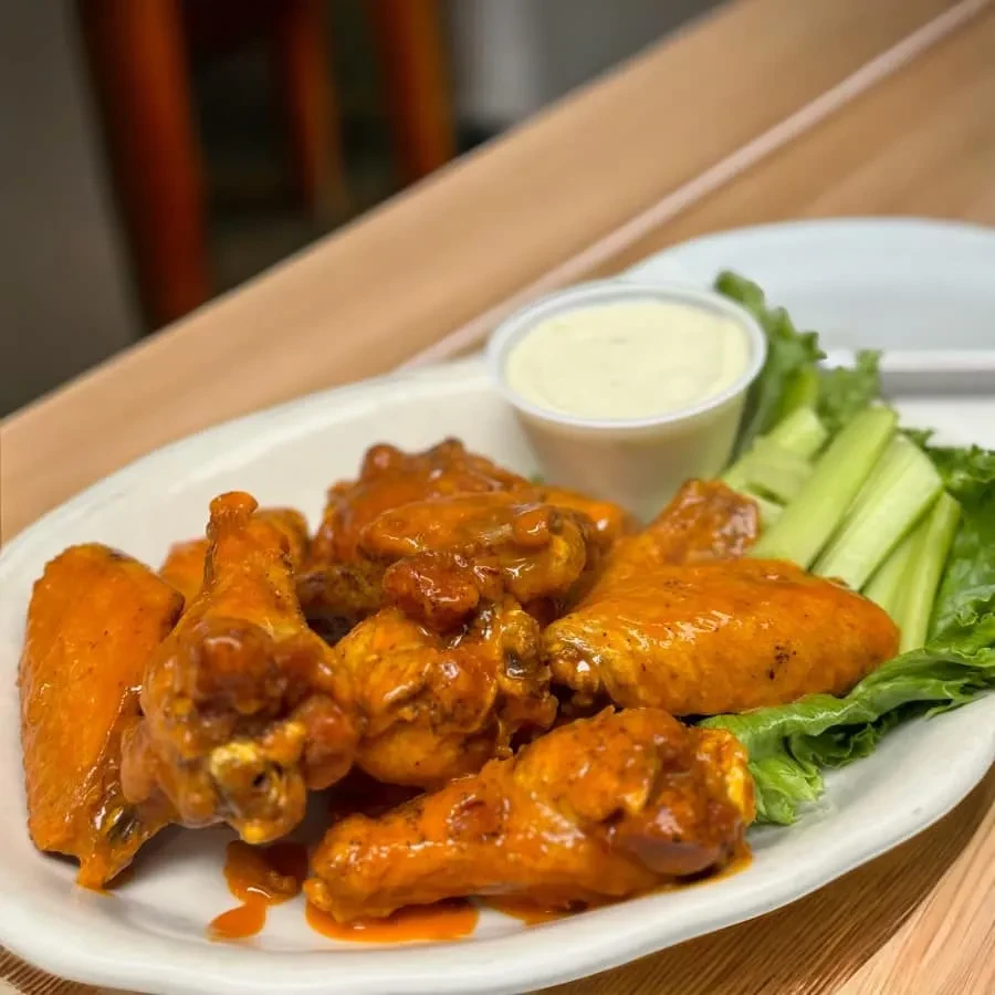 Plate of buffalo chicken wings with celery, lettuce, and creamy dip.