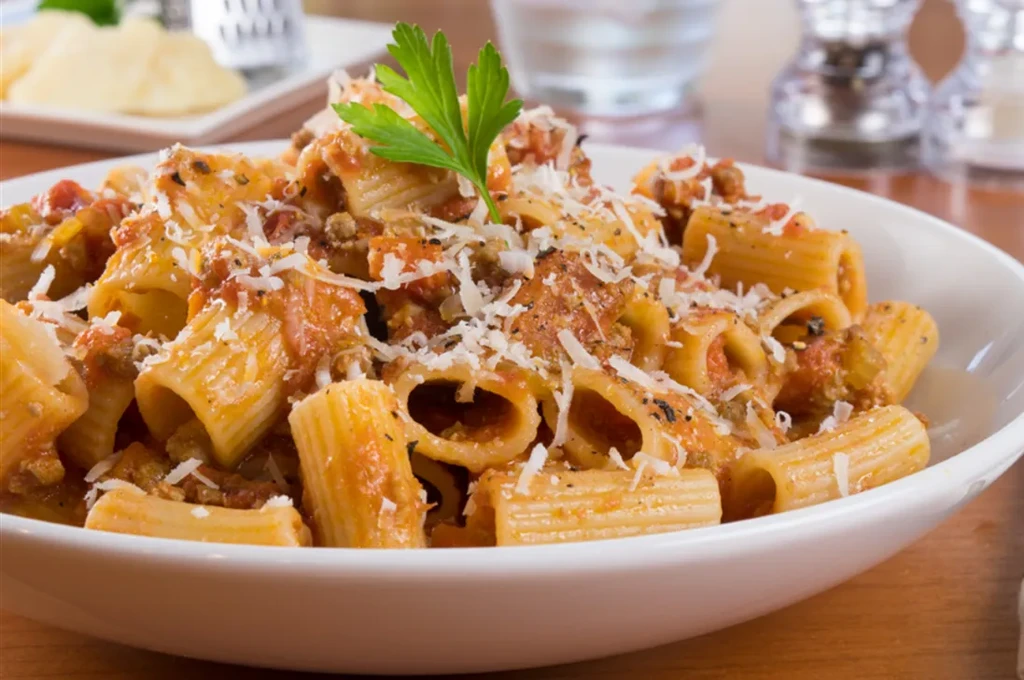 Rigatoni pasta with bolognese, parmesan cheese, and a parsley leaf.
