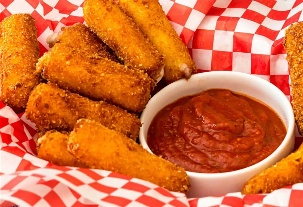 Golden-brown breaded sticks in a basket with red dipping sauce.