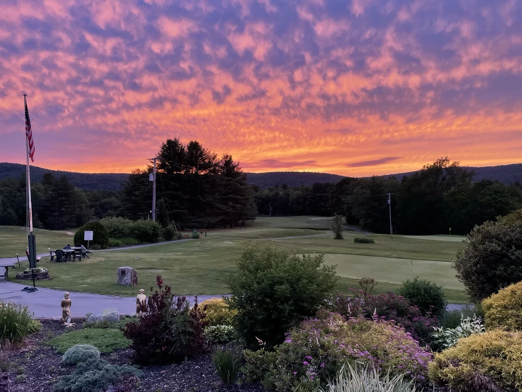 Vibrant sunset over a golf course with American flag and small statues.