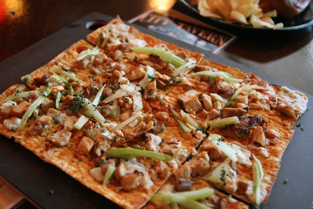 Chicken, cheese, and herb flatbread with red sauce on dark board.